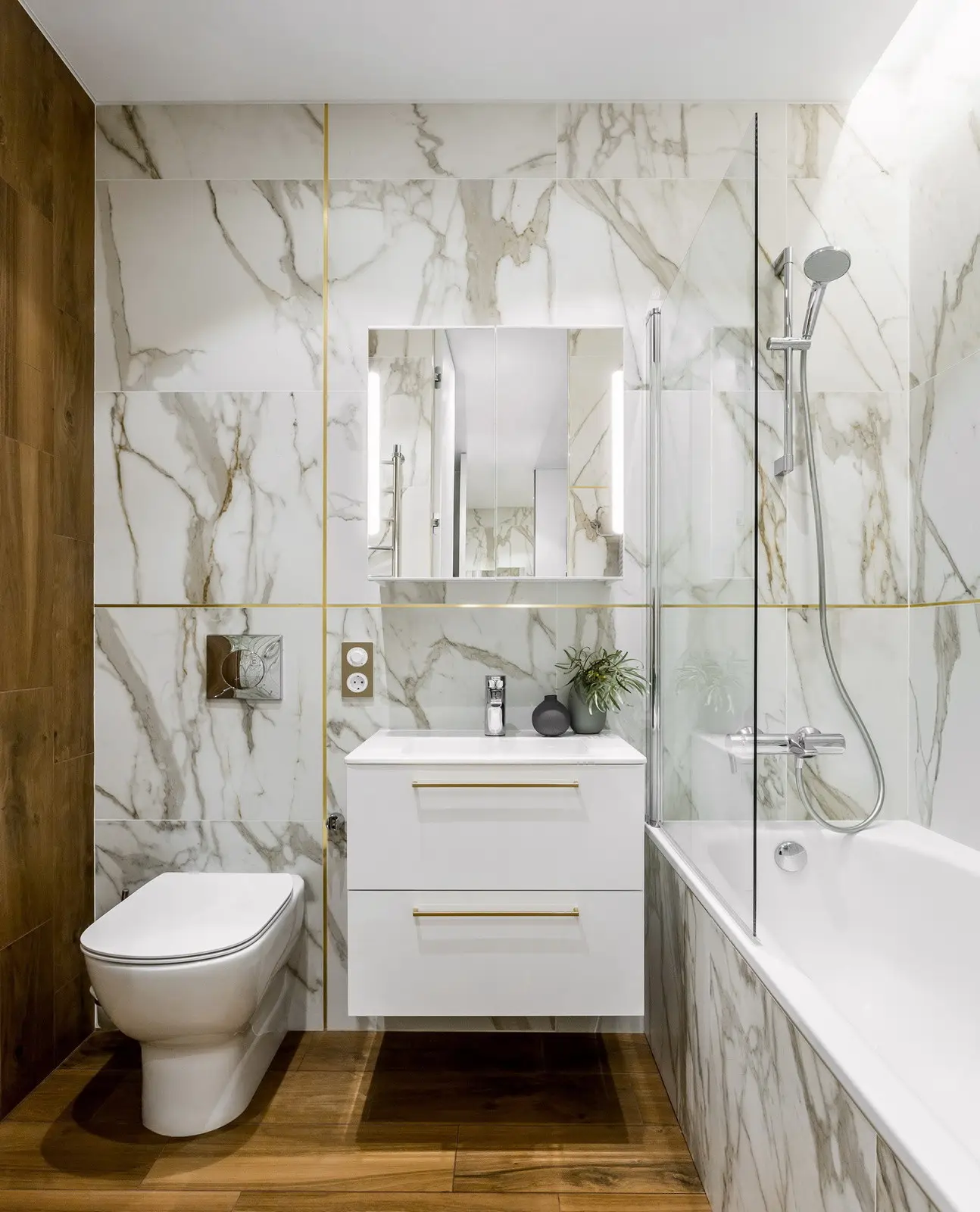 Floor-to-ceiling Calacatta marble porcelain wall tile in a modern bathroom with gold grout accents and bathtub