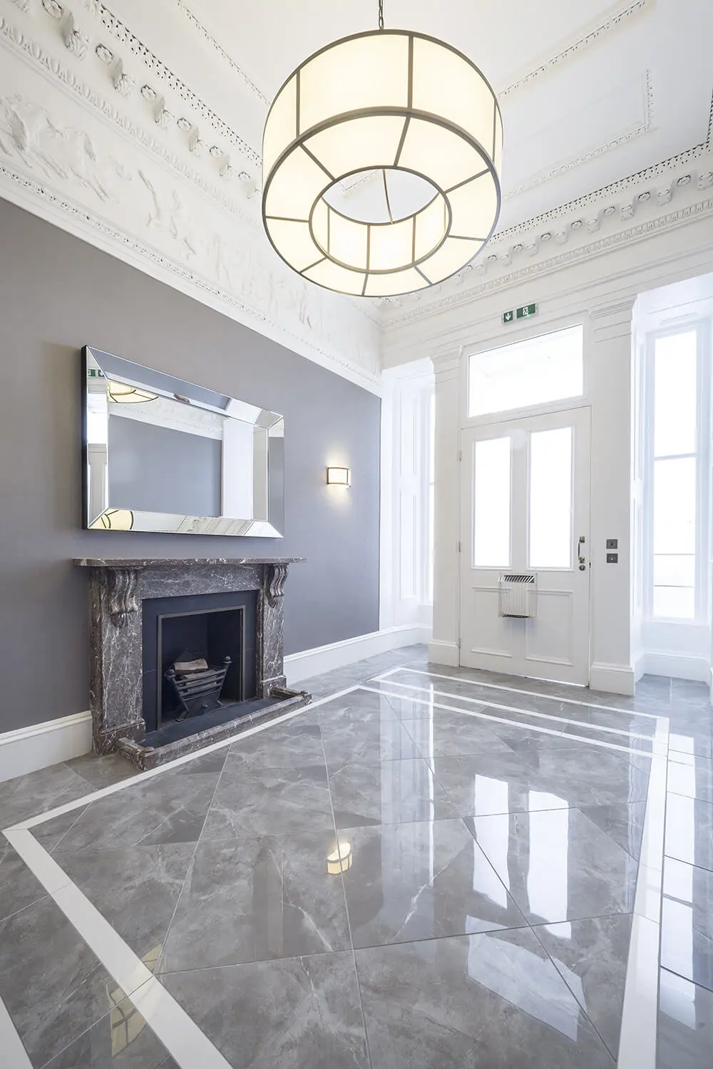 Polished gray marble-look porcelain tile installed in an elegant foyer with ornate ceiling and fireplace