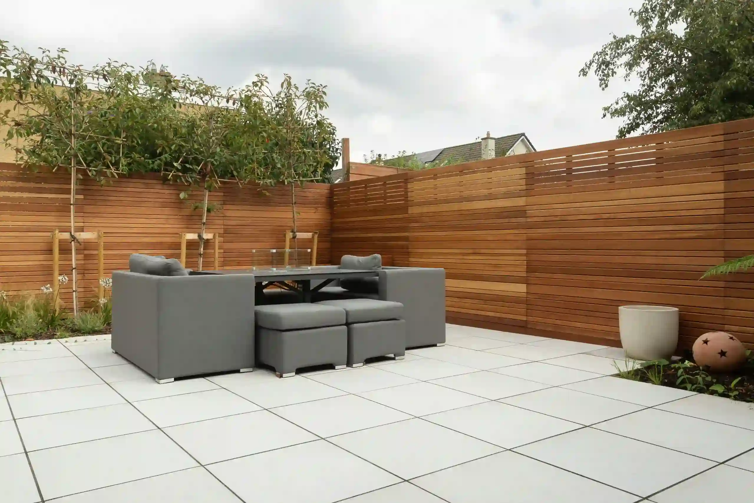 Large light gray porcelain pavers in a modern outdoor patio with wood fence and garden furniture